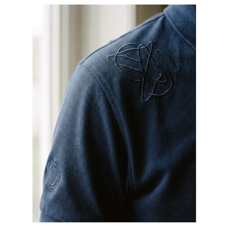 A tonal embroidered mark on a navy piqué polo, catching the light