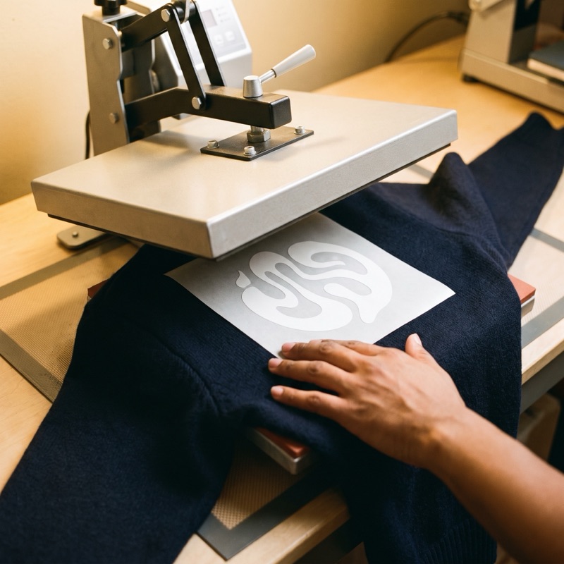 A heat press set over a vinyl mark on a navy sleeve