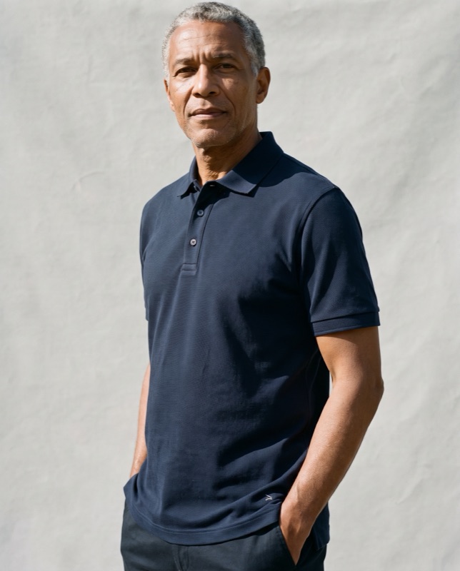 A model in a navy pique polo, hands in pockets, on a paper backdrop