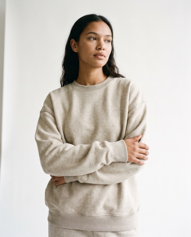 A model in an oatmeal crewneck sweatshirt, arms folded