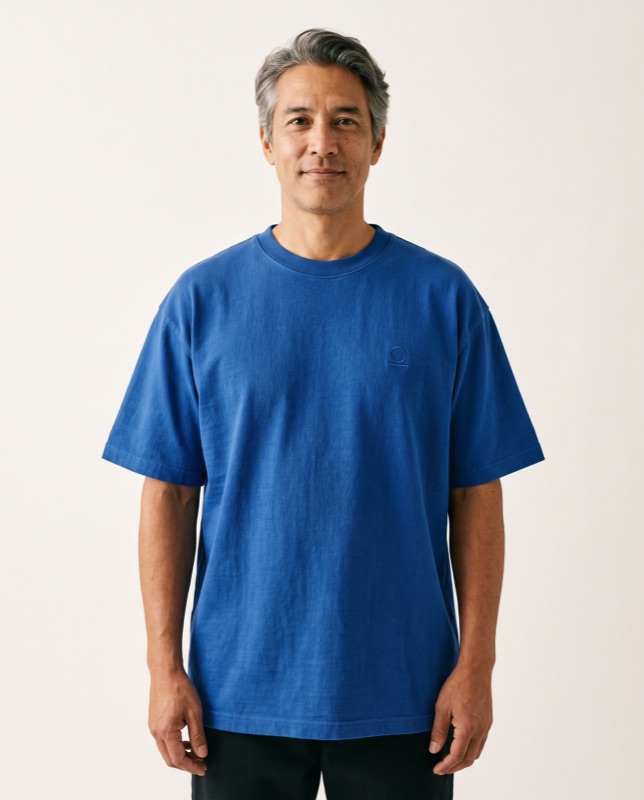 A model in a cobalt heavyweight tee against a warm paper backdrop
