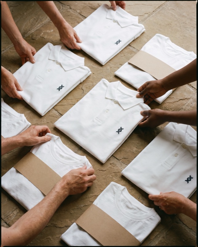 Flat lay of white piqué polos and white tees with a small navy helix, some wrapped in paper bands