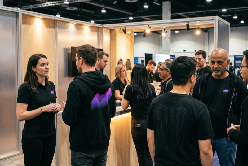 Northbeam Analytics staff on a trade show stand in black polos and tees, one in a black hoodie with an electric violet mark across the back